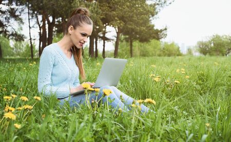young pretty girl working on laptop outdoors, sitting on grassの写真素材