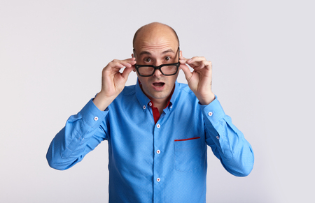Surprised handsome man looking at camera through the glasses. Isolated on greyの写真素材