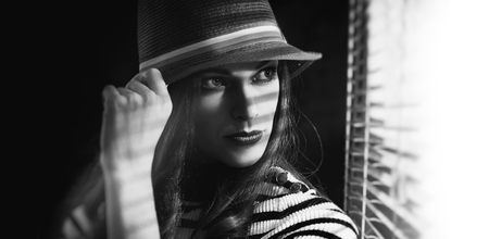 Black and white fashion portrait of beautiful elegant woman in hat looking at window. Retro style