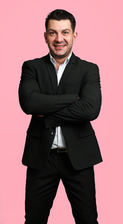 self-confident man in black suit with hands crossed. Handsome guy isolated on pink backgroundの写真素材