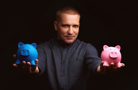 Man holding two piggy banks. handsome guy choosing bank for depositの写真素材