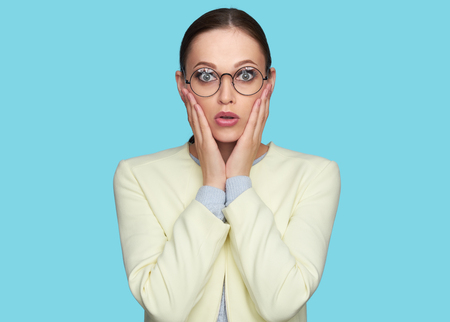shocked pretty girl. Surprised beautiful woman wearing glasses looking at camera. Isolated on blue
