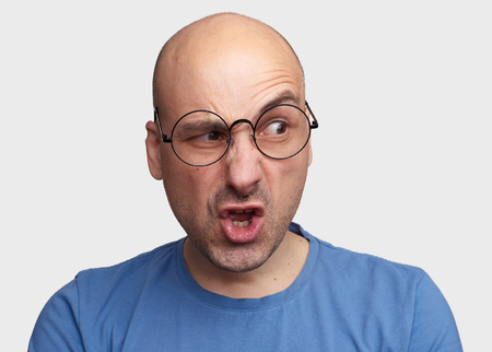 Portrait of man with silly grimace isolated over gray background. Bald guy looking with disgust at somebodyの写真素材