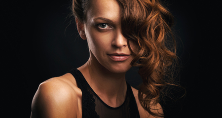 Beautiful girl with curly hairdo. Pretty woman with healthy wavy long hair. Black background