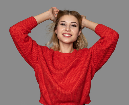 Portrait of a happy cheerful girl wearing a bright red sweater. Isolated on greyの写真素材