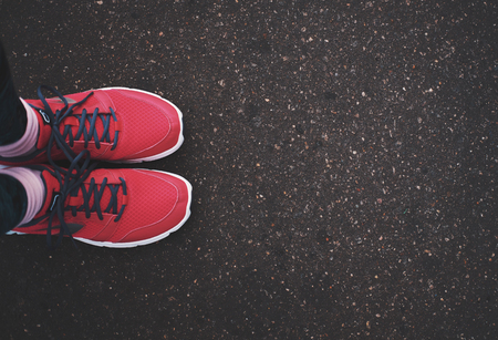 Feet in red sneakers on a asphalt road with copy space