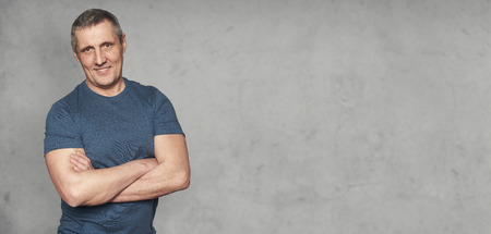 Handsome senior man is wearing t-shirt standing before grey stone studio wall