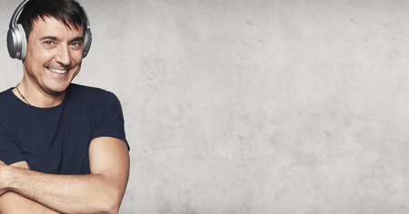 Happy man listening to music with headphones. Grey concrene studio wall with copy spaceの写真素材