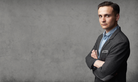 Portrait of young trendy man is standing before gray studio wall with copy spaceの写真素材