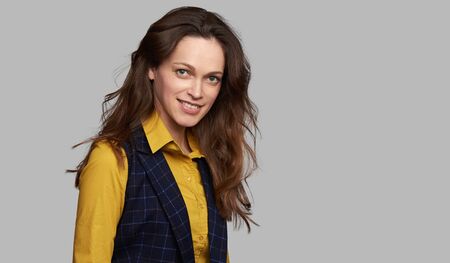 Beautiful woman with long brown hair is smiling. Isolated on grey studio wall