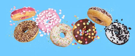 flying glazed round doughnuts. Mix of multicolored sweet donuts with sprinkles on blue backgroundの写真素材