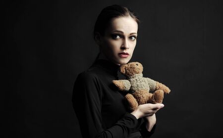 Sad young woman with a teddy bear. Black backgroundの写真素材