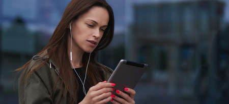 Pretty woman is listening to music with earphones and digital tablet. Outdoors portrait