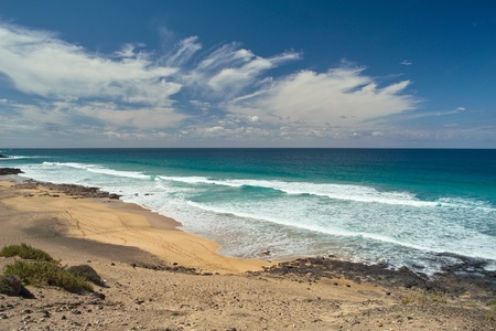 Green ocean waves, rocky beach and white clouds on horizon