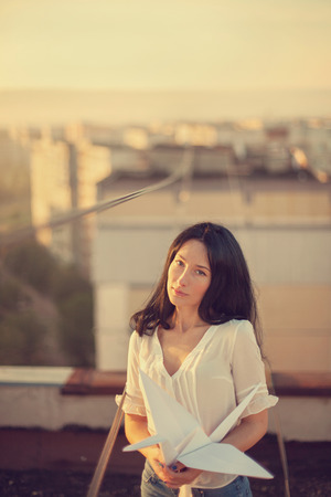Beautiful young girl at the roof with origami paper crane in hands. Vintage tinted, selective focus.の写真素材