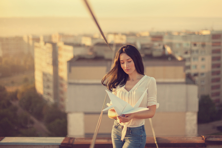 Beautiful young girl at the roof with origami paper crane in hands. Vintage tinted, selective focus.の写真素材