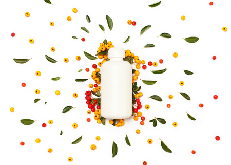 White plastic cosmetic bottle with green fresh leaves and yellow and red Pyracantha berries isolated on white background. Flat lay, top view.の写真素材