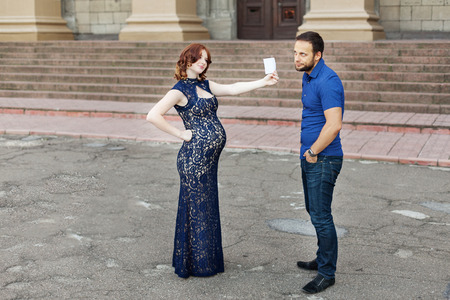 Funny image. Couple expecting a baby: woman holds a sign with space for text "boy" or "girl". Pregnancy in long dress. Future daddy in jeans and blue shirt.の写真素材