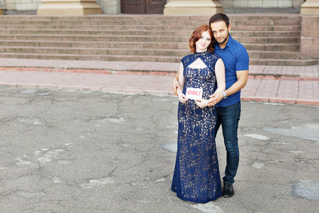Couple expecting a baby girl: pregnant mother holds a sign saying "girl!" Pregnancy in long dress. Future daddy in jeans and blue shirt.の写真素材
