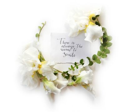 Floral frame wreath made of fresh Iris white flowers and green branches on white background. Flat lay, top view. Inspirational words There is always the reason to smile in calligraphy style.の写真素材