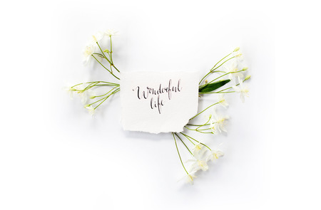 Minimalistic composition with words `Wonderful life` written in calligraphic style on paper with small white Clematis flowers frame on white background. Flat lay, top view.の写真素材