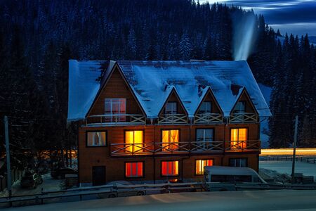 Night view of wooden snowy house with warm lights in windowsの写真素材