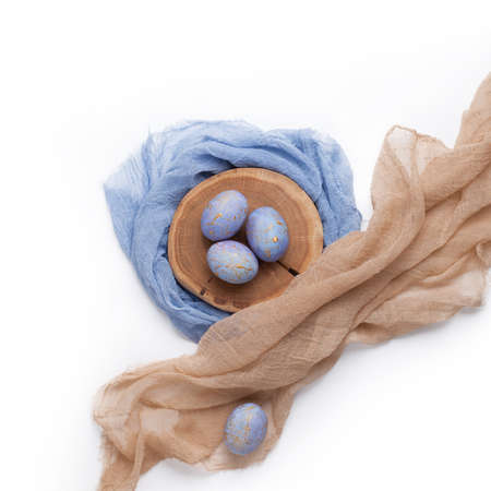 Happy Easter card. Gold and blue speckled easter eggs with pastel color textile and tree slice on white background.の写真素材