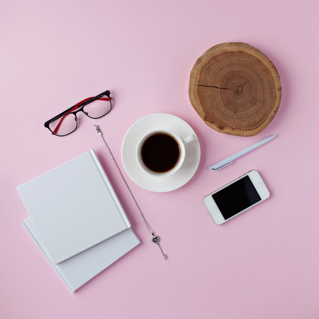 Creative flat lay arrangement with cup of cofee, notebook, mobile phone, branch on pink background. Top view workspace.の写真素材