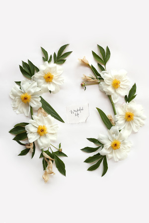 English quote Wonderful life handwritten in calligraphy style on paper in middle of floral frame with white peonies, leaves and buds. Flat lay, top view. の写真素材