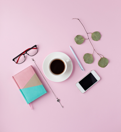 Creative flat lay arrangement with cup of cofee, notebook, mobile phone, branch on pink background. Top view workspace.の写真素材