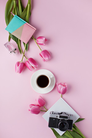 Workspace with old camera, tulips, cofee, notebook. Flat lay composition on pink background.の写真素材