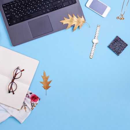 Home office workspace with laptop, glasses and dress on blue background. Fashion blogger work concept. Flat layの写真素材