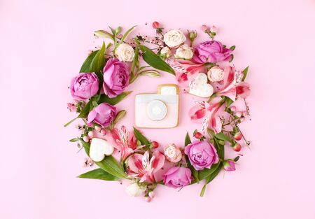 Photo camera shaped cookie on pink background. Rose buds and green leaves round frame wreath, flat lay, top view.の写真素材