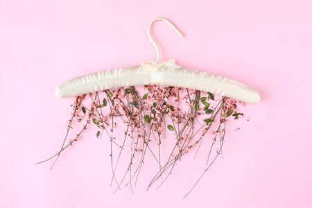 Clothes hanger with flowers on pink background. Flat lay, top view minimalistic composition.の写真素材
