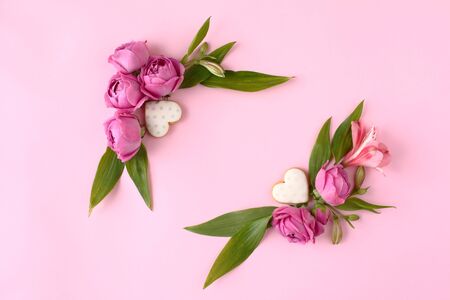Colorful rose buds and heart shaped cookies on pink background. Mock up frame with green leaves.の写真素材