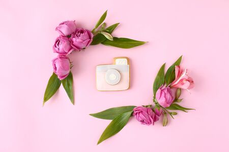 Colorful rose buds and camera cookie on pink background. Mock up frame with green leaves.の写真素材