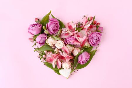 Heart shaped floral composition made of rose flowers, branches, leaves and cookies isolated on pink background. Flat lay, top view. Romantic concept.の写真素材