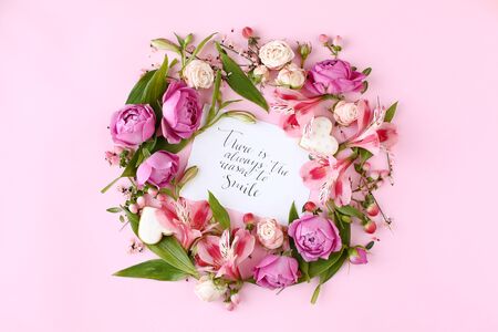 Card with calligraphic quote Â«There is always the reason to smileÂ» on pink background. Rose buds and green leaves round frame wreath, flat lay, top view.の写真素材
