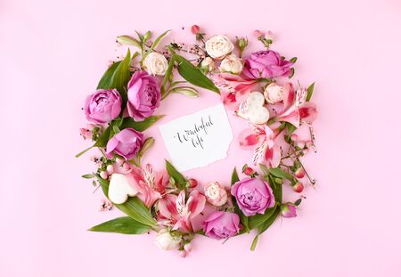 Card with calligraphic quote Â«Wonderful lifeÂ» on pink background. Rose buds and green leaves round frame wreath, flat lay, top view.の写真素材
