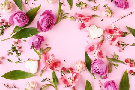 Frame of pink rose flowers, branches, leaves and heart shaped cookies with space for text on background. Flat lay, top view. Romantic concept.の写真素材