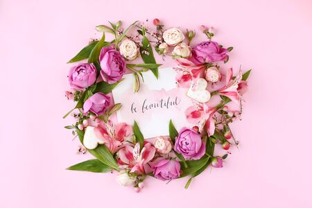 Card with calligraphic quote Â«Be beautifulÂ» on pink background. Rose buds and green leaves round frame wreath, flat lay, top view.の写真素材