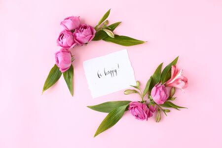 Card with calligraphic words Â«Be happyÂ« on pink background. Rose buds and green leaves frame, flat lay, top view.の写真素材