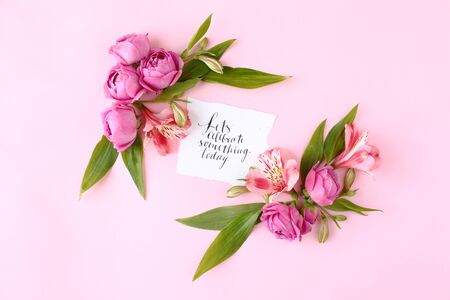 Card with calligraphic quote Â«Letâs celebrate something todayÂ» on pink background. Rose buds and green leaves frame, flat lay, top view.の写真素材