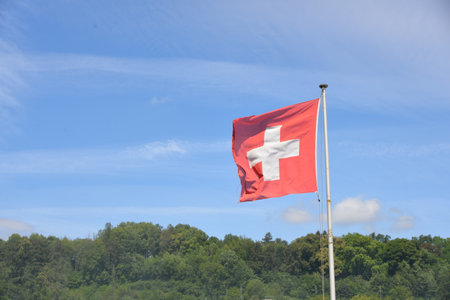 Swiss flag waving in the wind on a background of blue skyの写真素材
