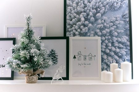 Christmas frames are next to a decorative Christmas tree and candles on the windowsill