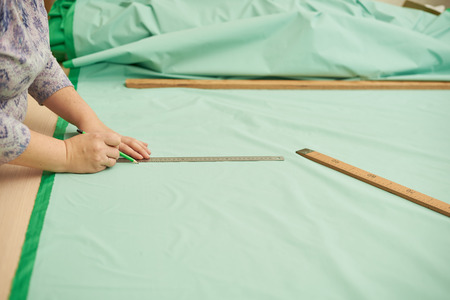 Woman cut out material green pencil for clothing. Green material lies on the table.