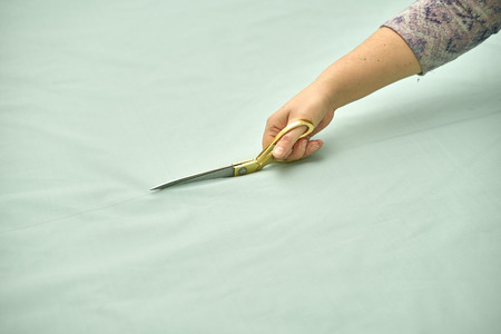 Woman cuts green material with Golden scissors. Roll of material lying on the table.