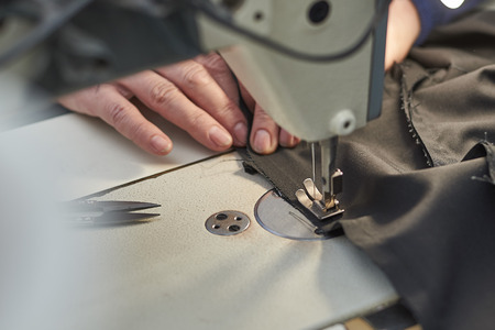A woman sews on an electric sewing machine. Black material. Smooth seam.