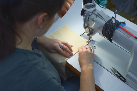 A woman sews on an electric sewing machine. Black material. Smooth seam.