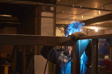 welder welds a metal frame for the power plant. The man works in a protective mask.